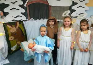 Aniołki, Maryja i Józef stoją przy stajence.